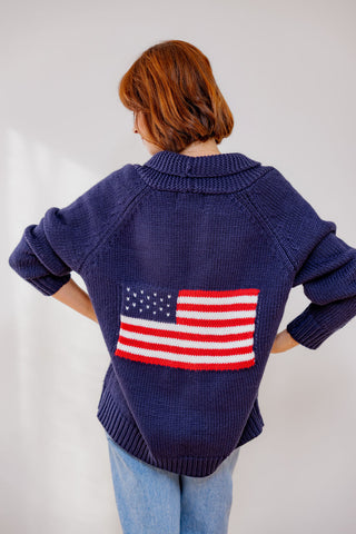 Person wearing a navy blue sweater with an American flag on the back against a white background