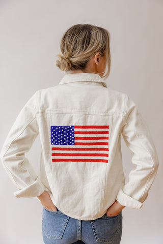 Person wearing a white jacket with an American flag patch on a plain background