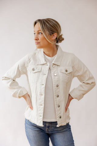Woman wearing a beige denim jacket and blue jeans against a plain background